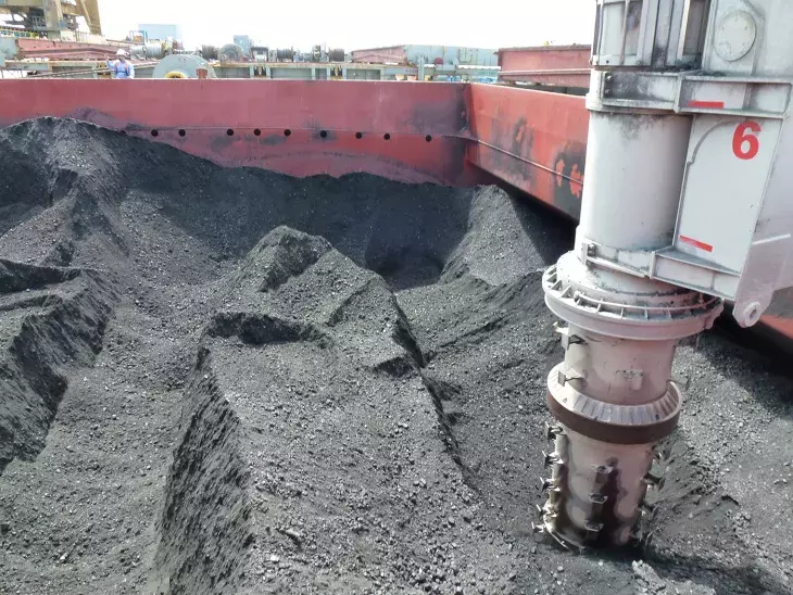 Closeup of inlet feeder and vertical arm of ship unloader unloading coal in ship hold